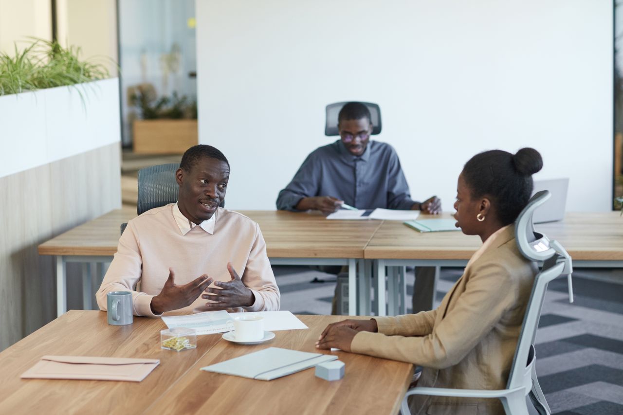 Three professionals engaging in a meeting at an indoor office workspace.